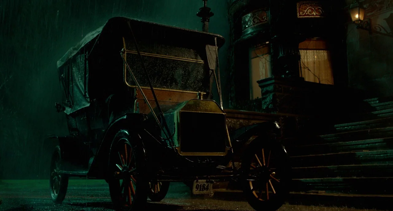 Crimson Peak (2015) movie still: fullbody — A rain-slicked driveway shows an antique Ford Model T parked beside a stone mansion. Heavy rain falls…