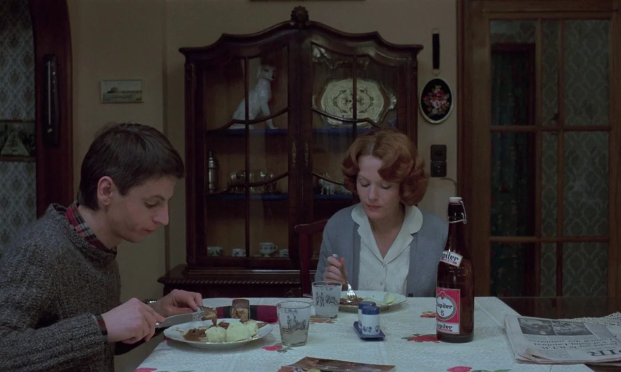 Jeanne Dielman, 23, quai du commerce, 1080 Bruxelles (1975) movie still: medium — A domestic dining area featuring a dark wood cabinet and a floral…