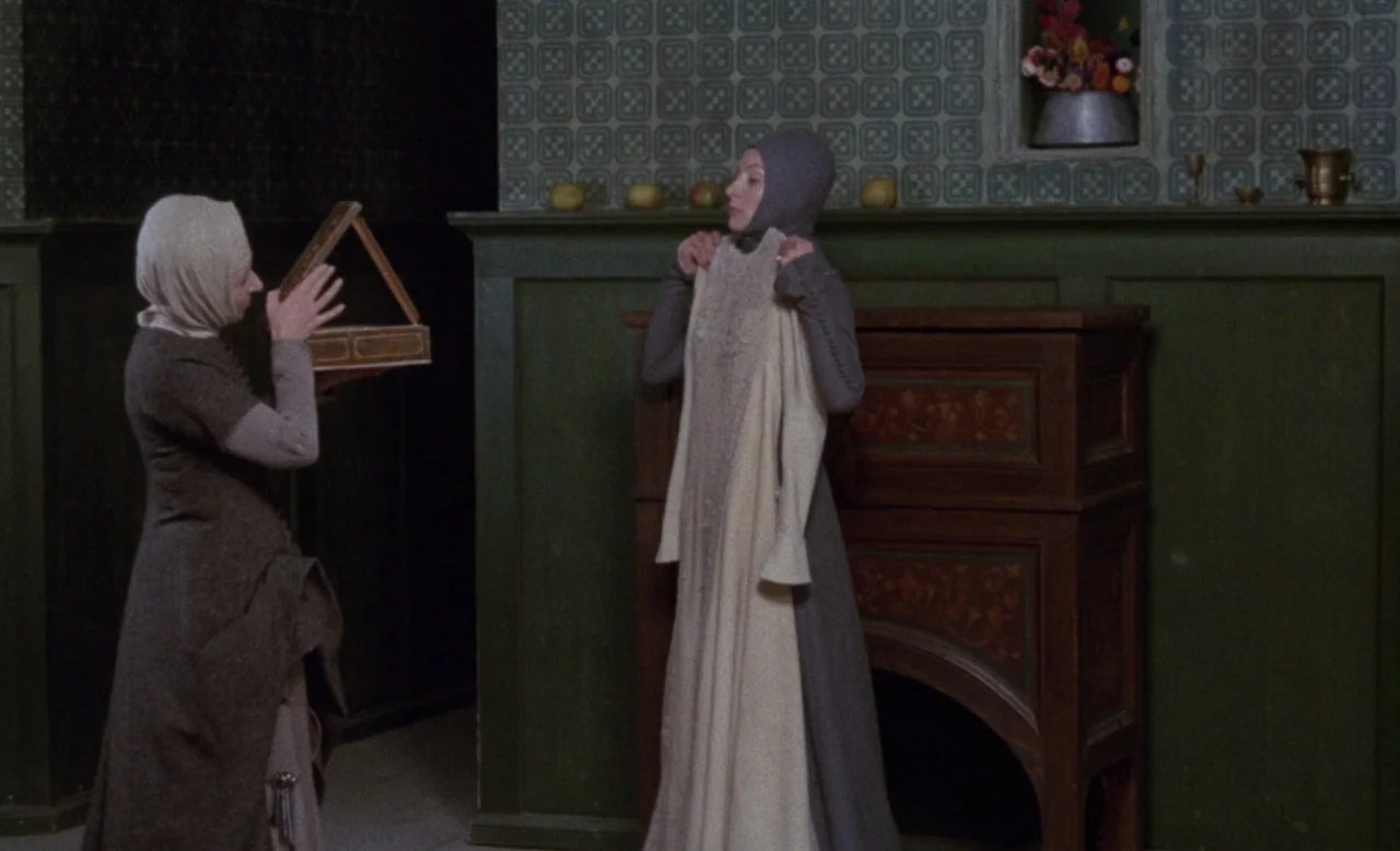 Blanche (1971) movie still: fullbody — A stone chamber features dark green wainscoting and patterned wallpaper above a fireplace mantel. Two women…