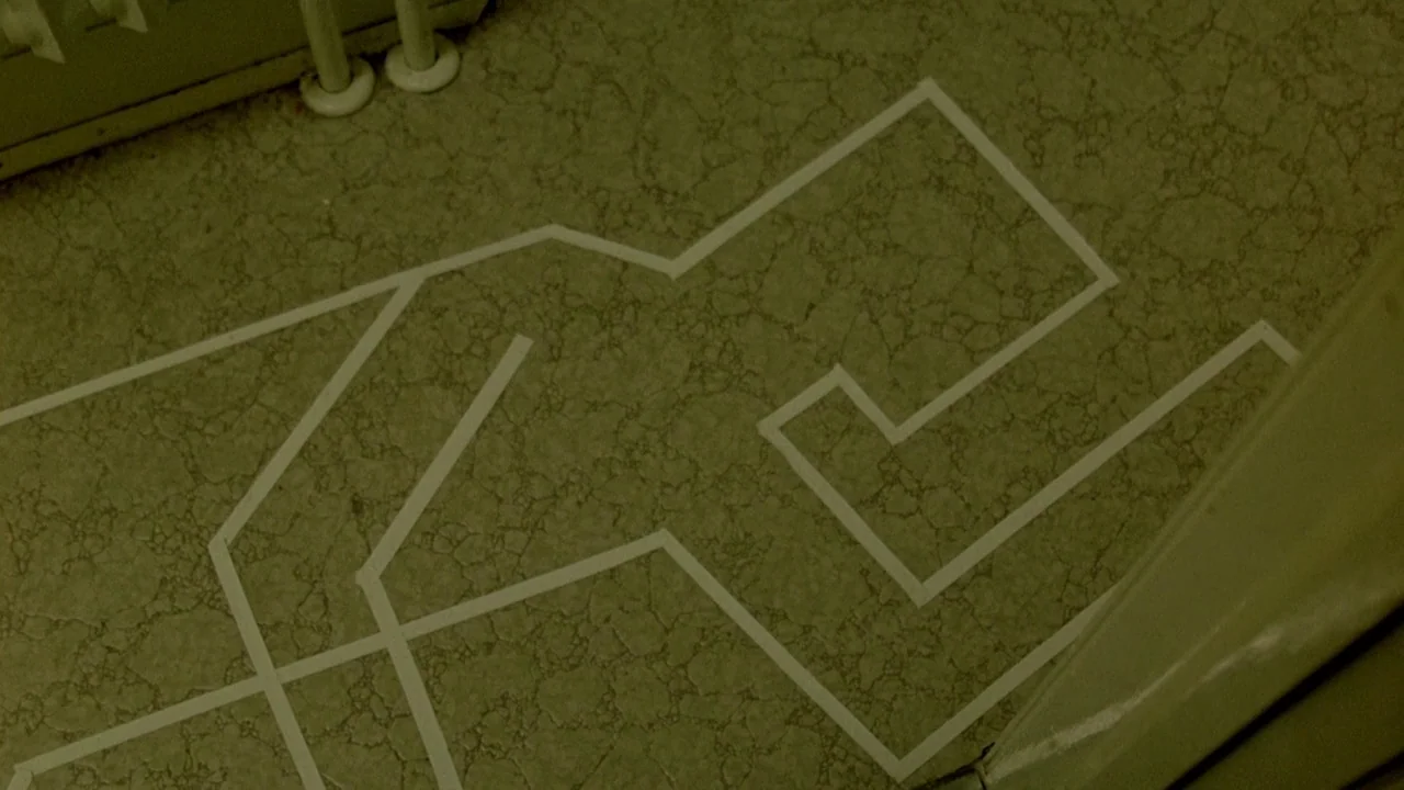 The Brood (1979) movie still: closeup — A speckled vinyl floor features a white tape outline shaped like a human body. The surface has a dull,…