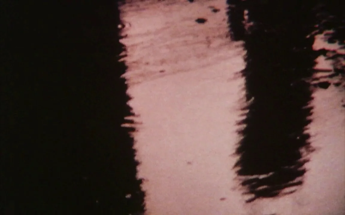 The Last of England (1987) movie still: closeup — The frame depicts a close-up of dark water surface with shimmering light reflections. Jagged,…