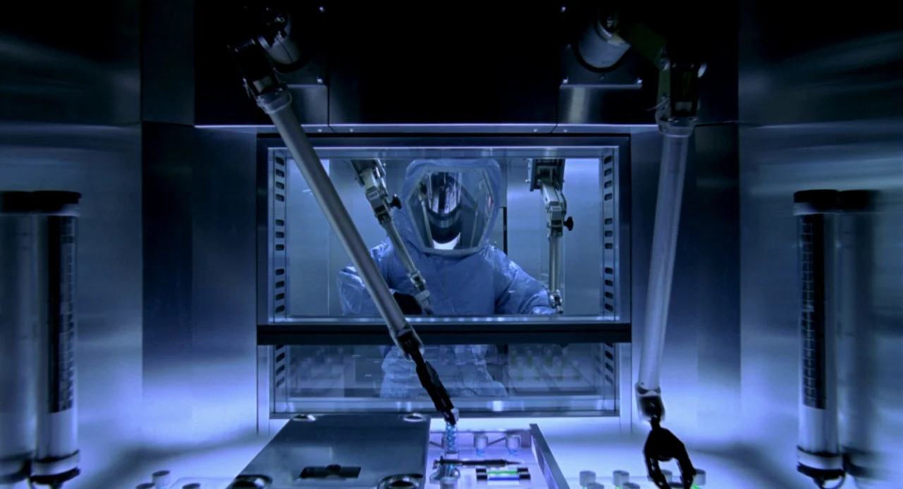 Resident Evil (2002) movie still: medium — A sterile laboratory glovebox chamber is constructed from polished stainless steel and thick glass. A…