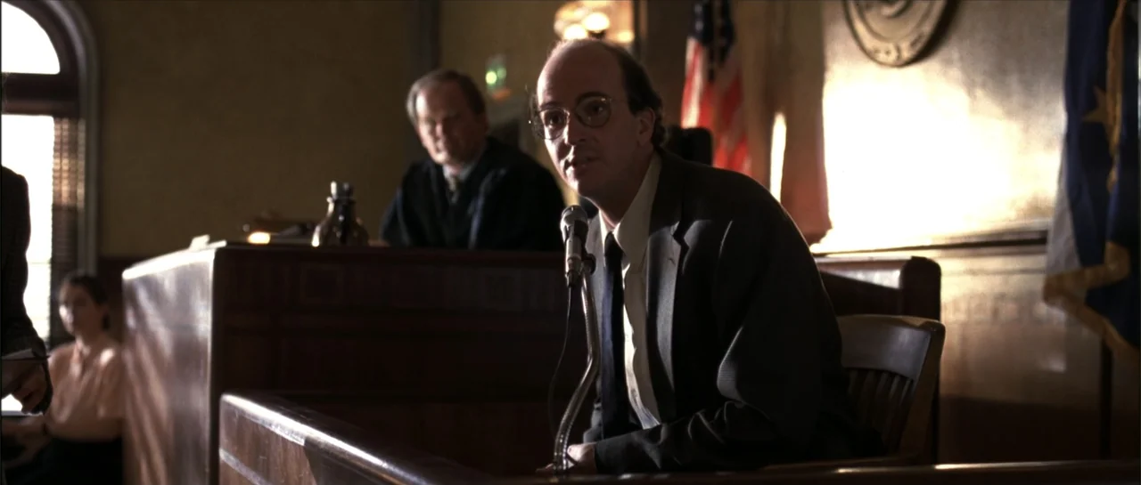 Gang Related (1997) movie still: medium — A wood-paneled courtroom features a judge sitting at a bench in the background. A man in a suit sits at…