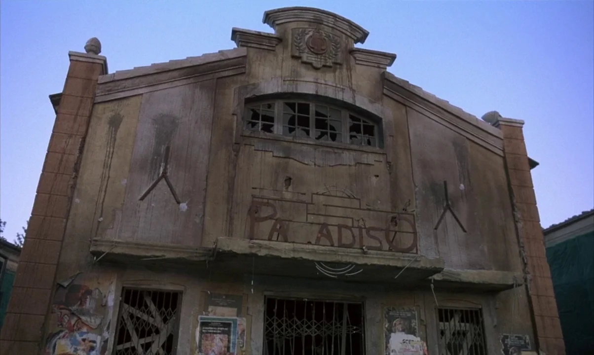 Cinema Paradiso (1988) movie still: establishing — A weathered, abandoned cinema building features a cracked facade and a partially missing sign.…