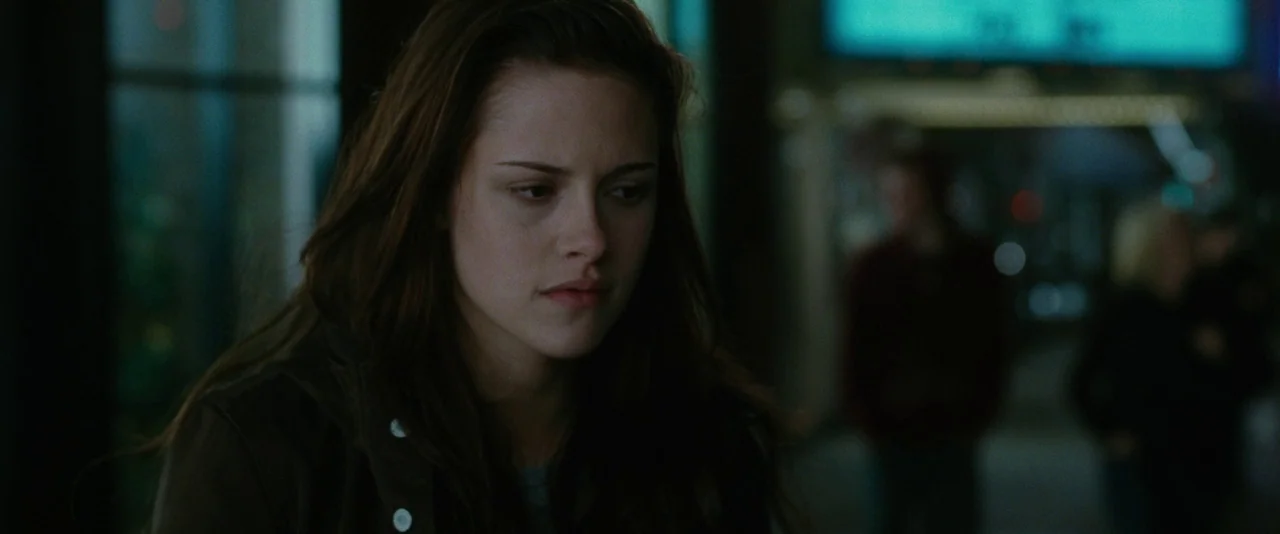 The Twilight Saga: New Moon (2009) movie still: closeup — A woman stands on a dark city street at night with blurry lights behind her. She looks…