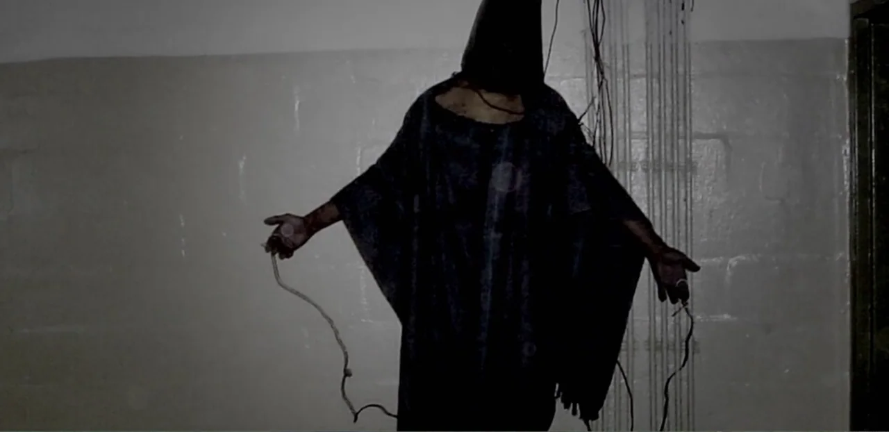 Doctors of the Dark Side (2011) movie still: medium — A dark, spartan industrial space features blank walls and overhead cabling. A hooded figure…