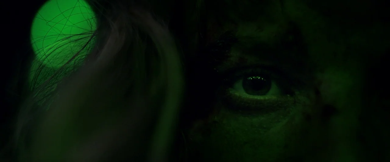 Meanwhile On Earth (2024) movie still: closeup — A close-up of a human eye in a dark environment. The face is partially lit by a bright green glow.