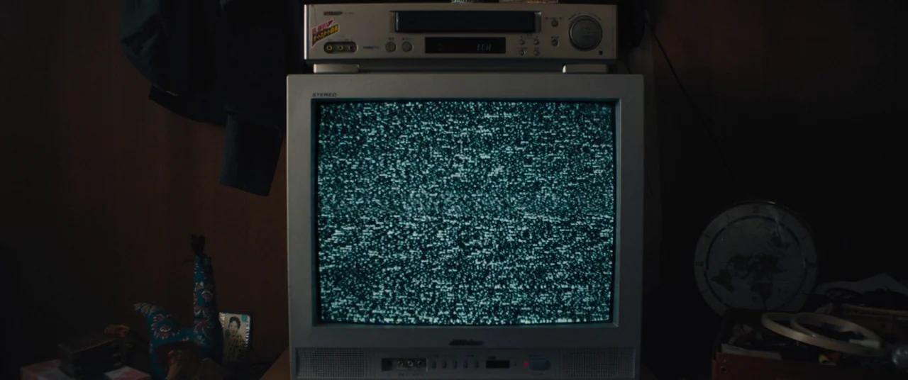 Kumiko the Treasure Hunter (2014) movie still: closeup — A silver cathode-ray tube television sits on a surface with a VCR on top. The screen is…