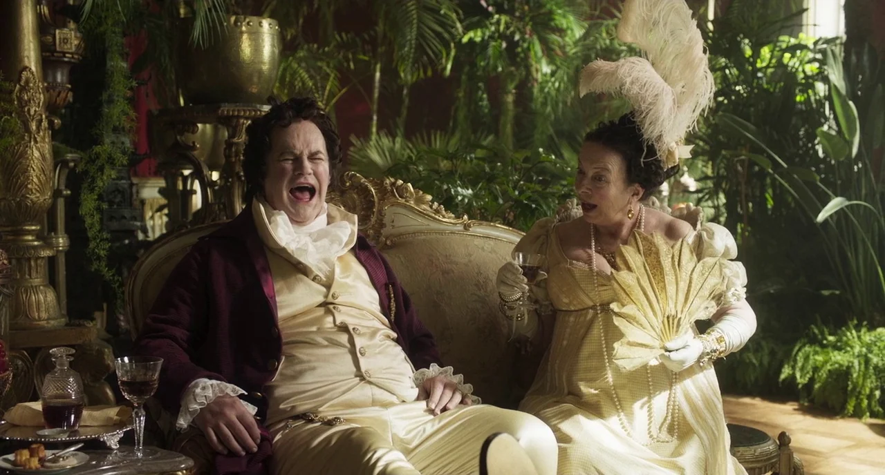 Peterloo (2018) movie still: medium — An opulent 19th-century parlor is densely packed with large tropical potted plants and gold furniture. A man…