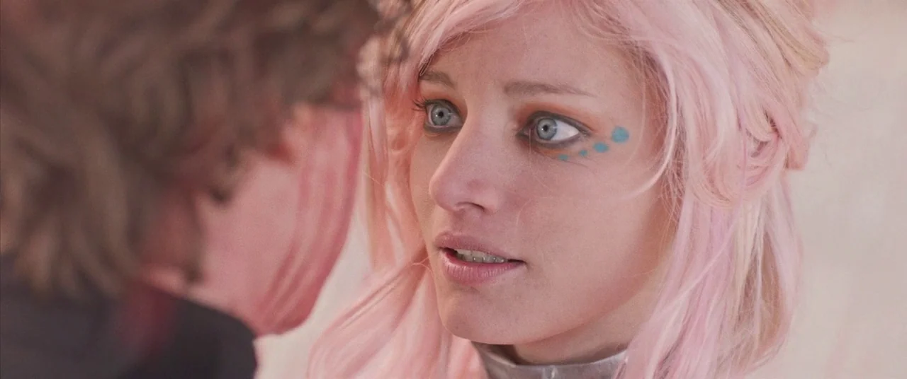 Turbo Kid (2015) movie still: closeup — A light-colored interior setting frames a close encounter between two individuals. A woman with light pink…