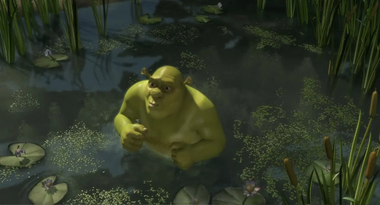 Shrek (2001) movie still: medium — A murky, green-tinted swamp is filled with lily pads and tall reeds. A green ogre stands waist-deep in the water,…