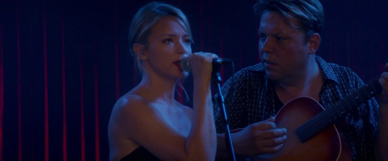 Sibyl (2019) movie still: medium — A dark performance area featuring vertical red light bars in the background. A woman sings into a handheld…