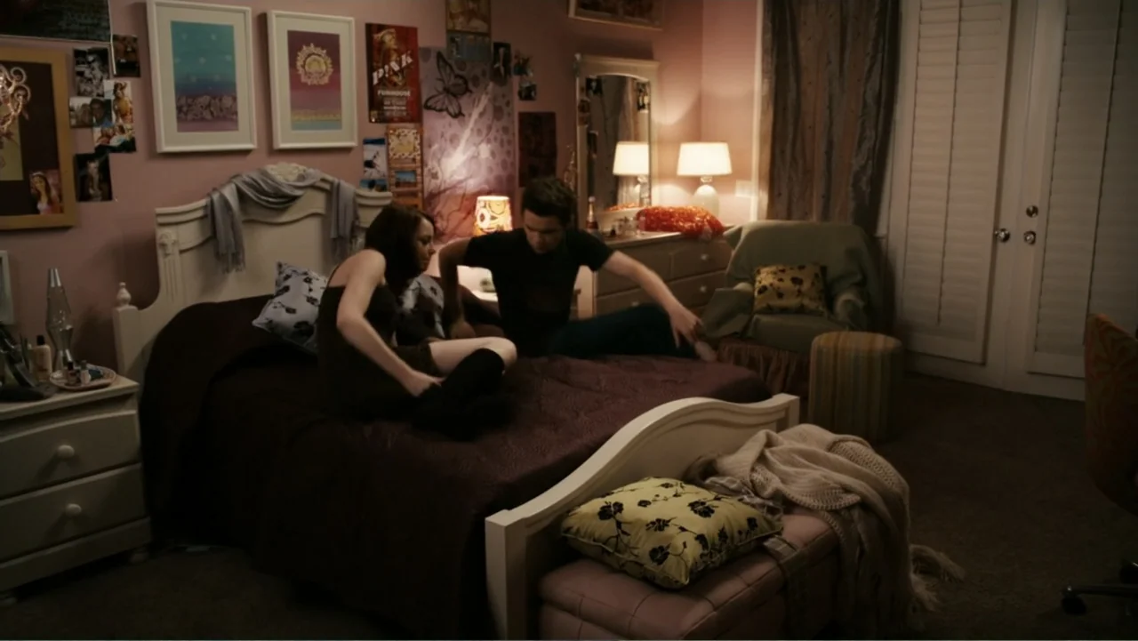 Easy A (2010) movie still: medium — A teenage bedroom features pink walls decorated with posters and a large white headboard. A young couple sits…