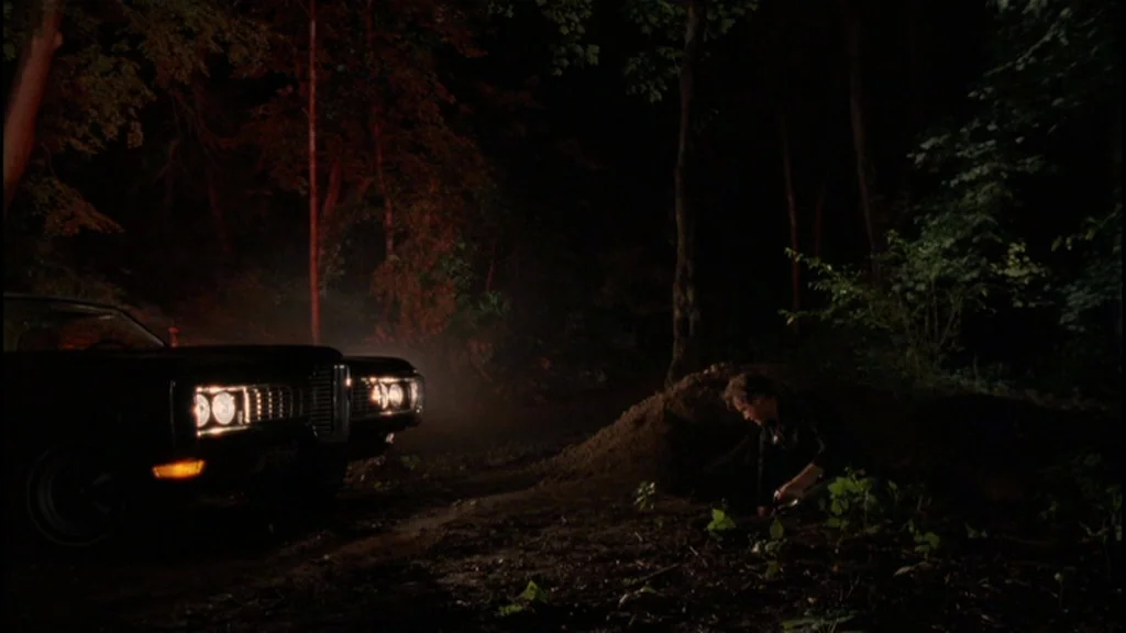 Goodfellas (1990) movie still: wide — A dark, wooded clearing at night features a mound of freshly turned dirt. A man kneels beside the hole while…