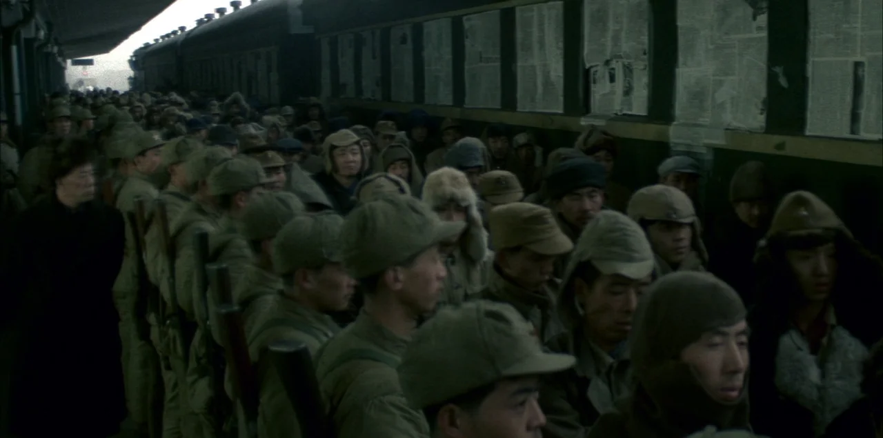 The Last Emperor (1987) movie still: wide — A crowded train platform features soldiers packed tightly together beside a long, dark train car. The…