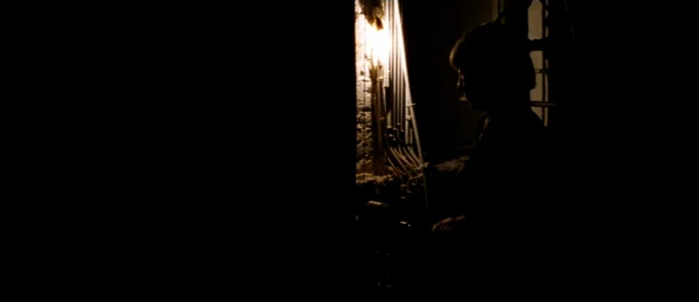 Innocence (2005) movie still: medium — A dimly lit utility area features exposed conduit pipes running vertically along a wall. A dark silhouette of…