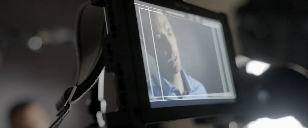 I Choose to Believe (2023) movie still: medium — A digital camera monitor displays a close-up image of a man on a film set. The man in the blue…