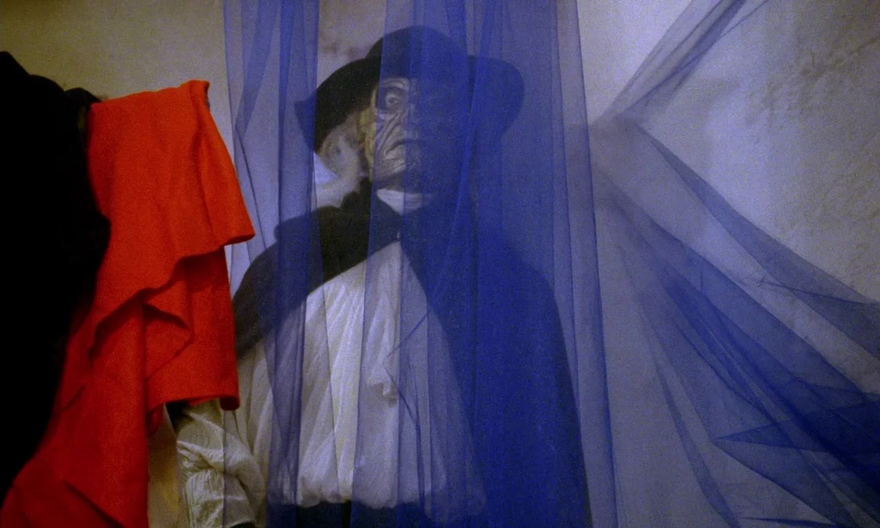 Paganini Horror (1989) movie still: medium — A dimly lit space features a figure standing behind several layers of blue netting. The figure wears an…