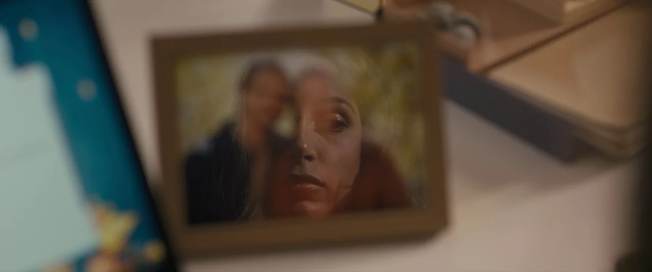 Intrusion (2021) movie still: closeup — A framed photograph rests on a white desk surface near other office supplies. The image inside the frame…