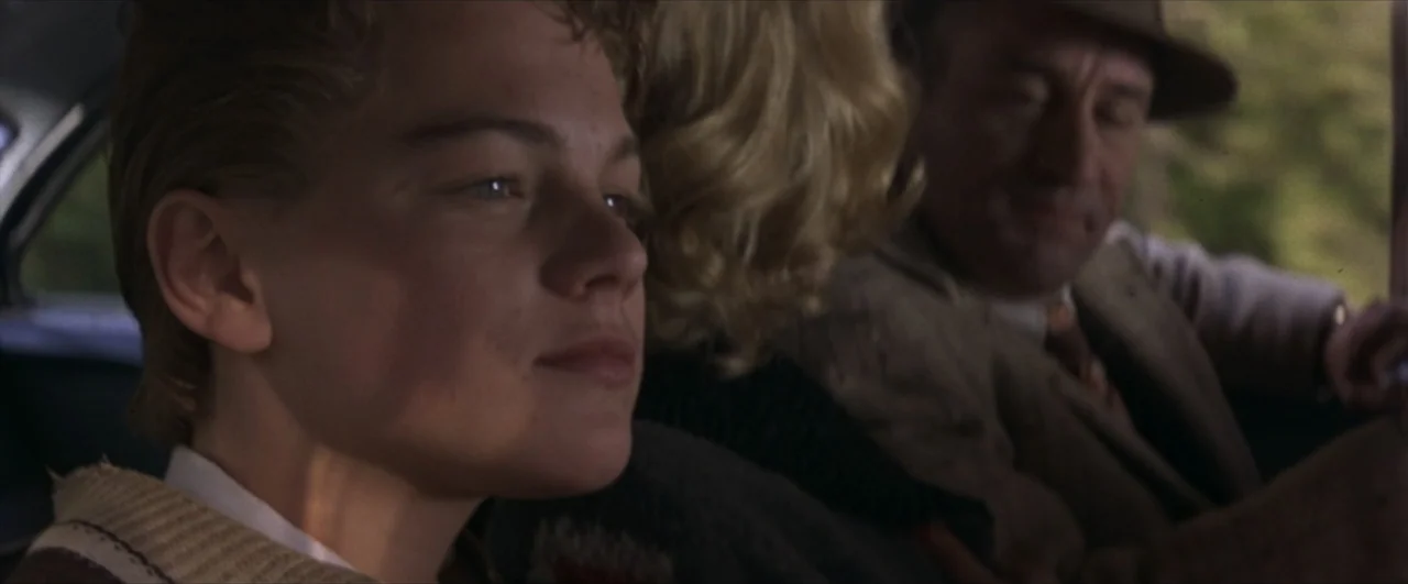 This Boy's Life (1993) movie still: medium — Three people sit inside the cabin of a moving vintage automobile during the day. A teenage boy looks…