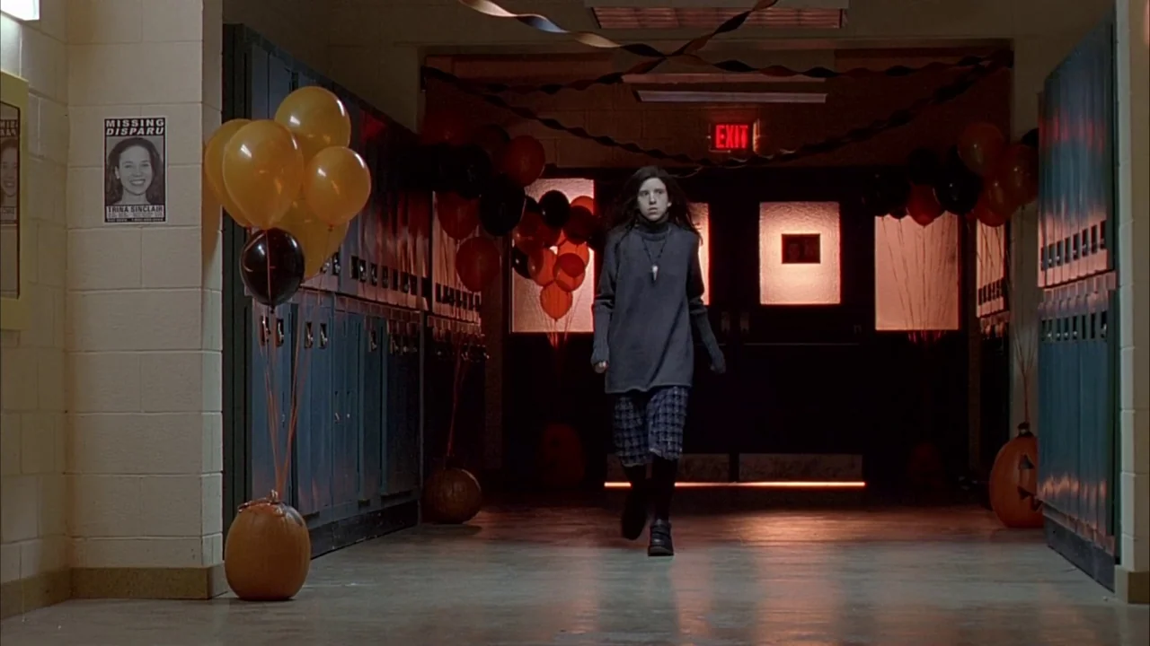 Ginger Snaps (2000) movie still: fullbody — A school hallway decorated with orange and black balloons for an event. A young woman walks toward the…