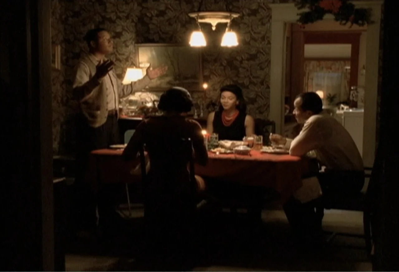 Boycott (2001) movie still: medium — A vintage dining room features floral wallpaper and a table set for dinner. Three adults sit at a table while a…