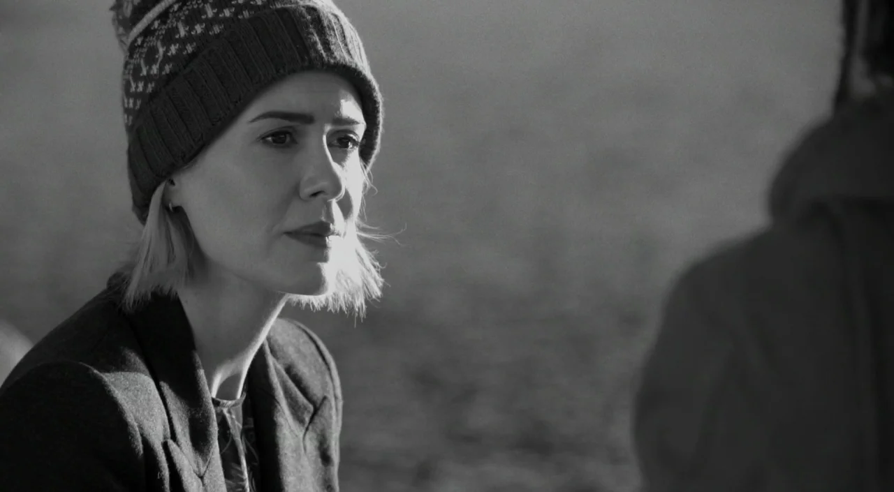 Blue Jay (2016) movie still: closeup — A woman stands outdoors in a bright, desaturated environment with a sandy or textured background. She turns…