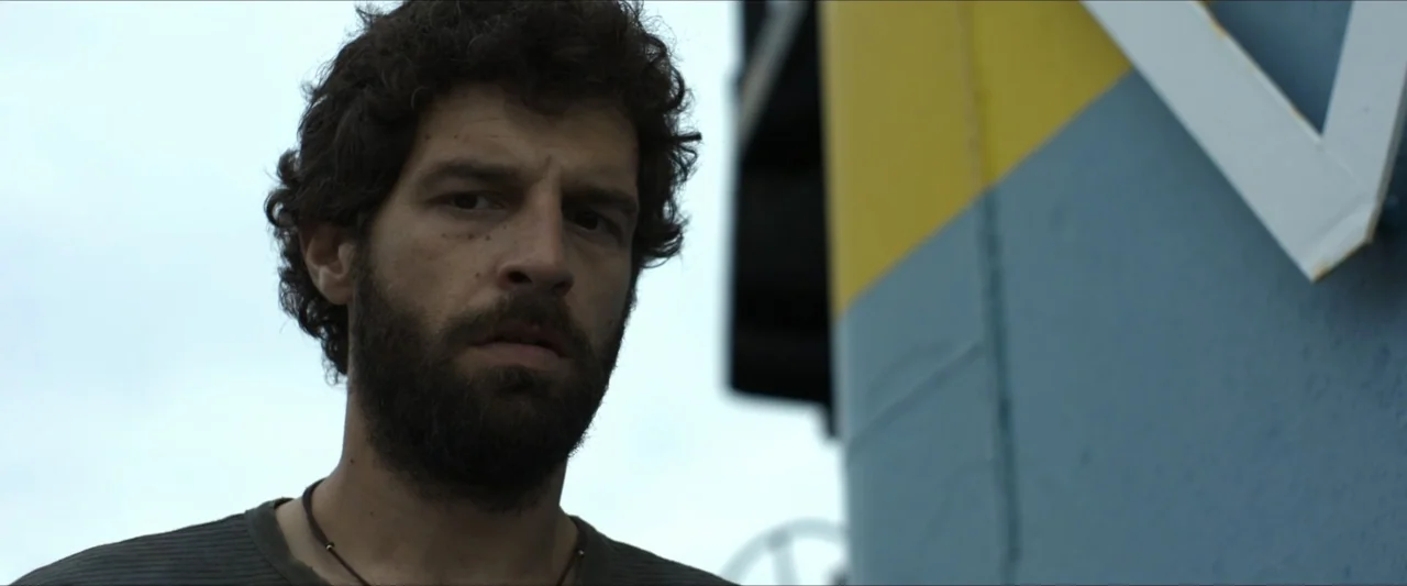 Apocalypse Z: The Beginning of the End (2024) movie still: closeup — An outdoor location near a structure with blue and yellow painted surfaces. A…