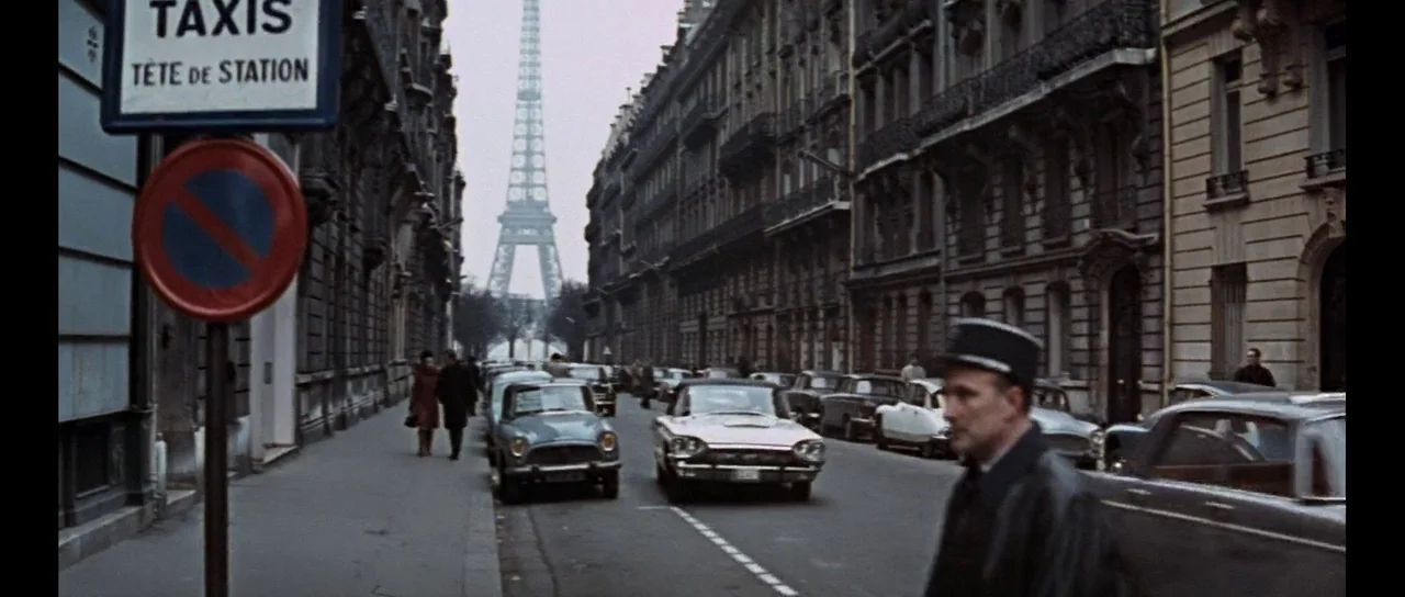 Thunderball (1965) movie still: wide — A Paris street scene features a distant view of the Eiffel Tower framed centrally. Vintage cars drive down…