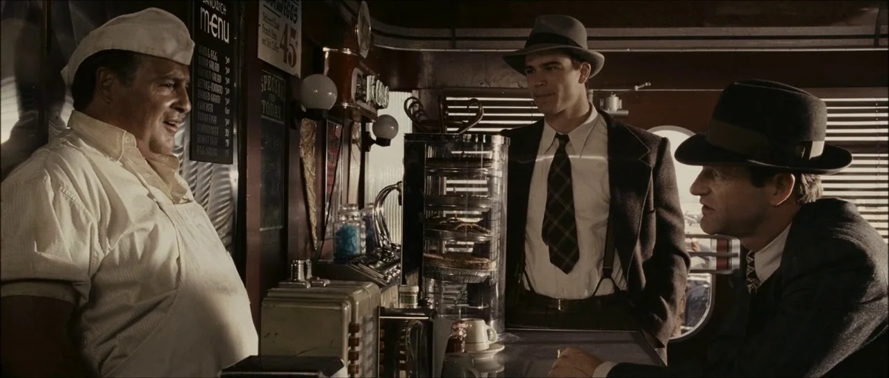 The Black Dahlia (2006) movie still: medium — A classic 1940s diner features metal trim and a glass pastry case. Two men in fedoras converse with…