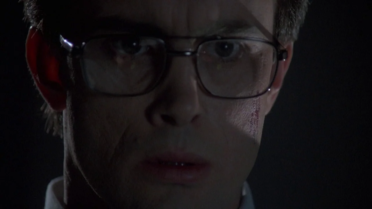 Re-Animator (1985) movie still: closeup — A man stands in an undifferentiated dark environment with no visible architectural features. He faces the…