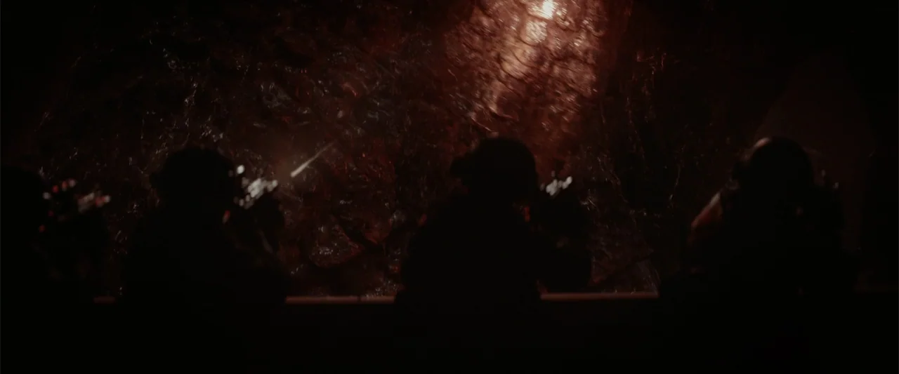 Godzilla (2014) movie still: medium — A dark, cavernous space features a rough organic wall with wet, glistening texture. Three soldiers wearing…