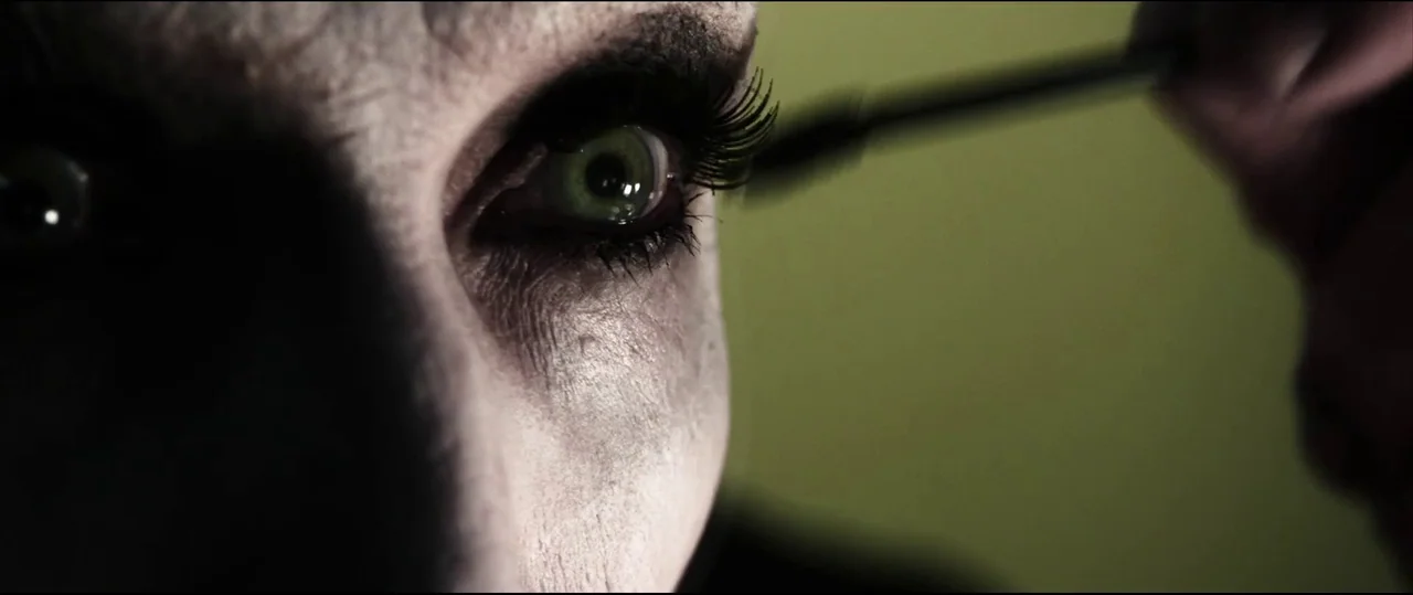 Insidious: Chapter 2 (2013) movie still: closeup — A close-up view focuses on a pale face with dark makeup against an olive background. The subject…