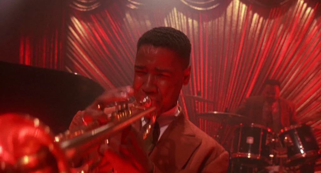 Mo’ Better Blues (1990) movie still: medium — A dimly lit jazz club features a red-curtained background with vertical pleated fabric. A man in a…