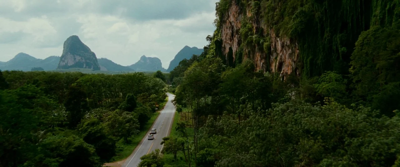 The Hangover Part II (2011) movie still: wide — A rural asphalt road winds through a lush tropical landscape with dramatic limestone karsts. Two…