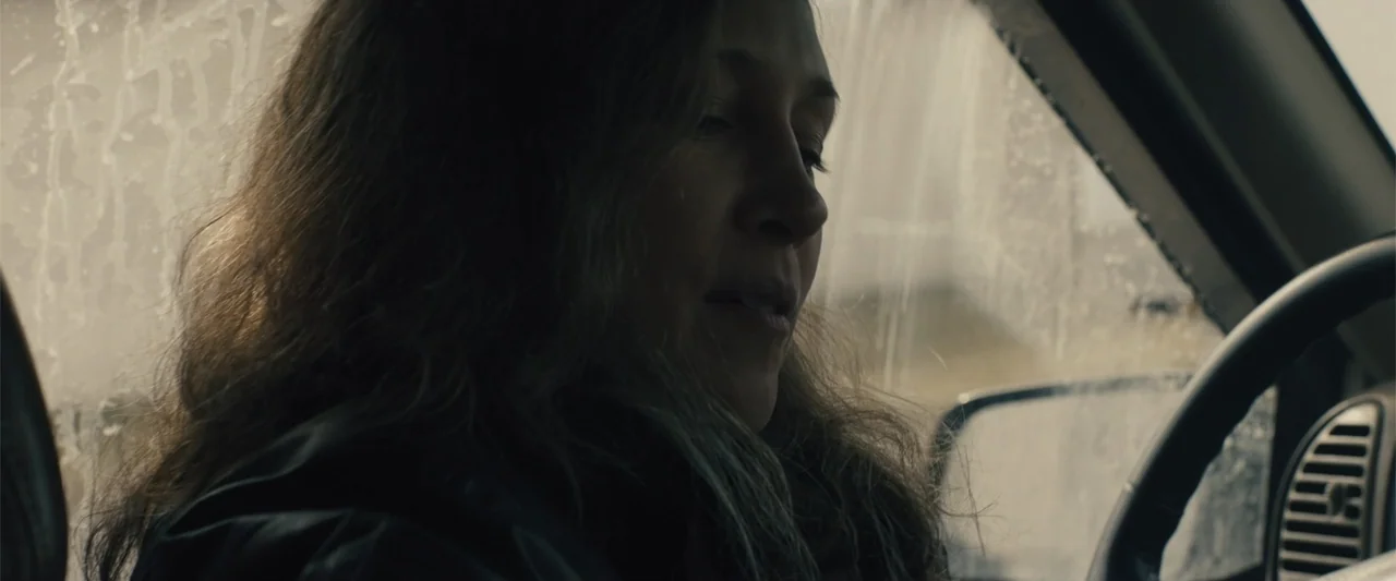 Skin (2009) movie still: closeup — The interior of a vehicle on a rainy day features rain-streaked glass. A woman sits in the driver's seat looking…