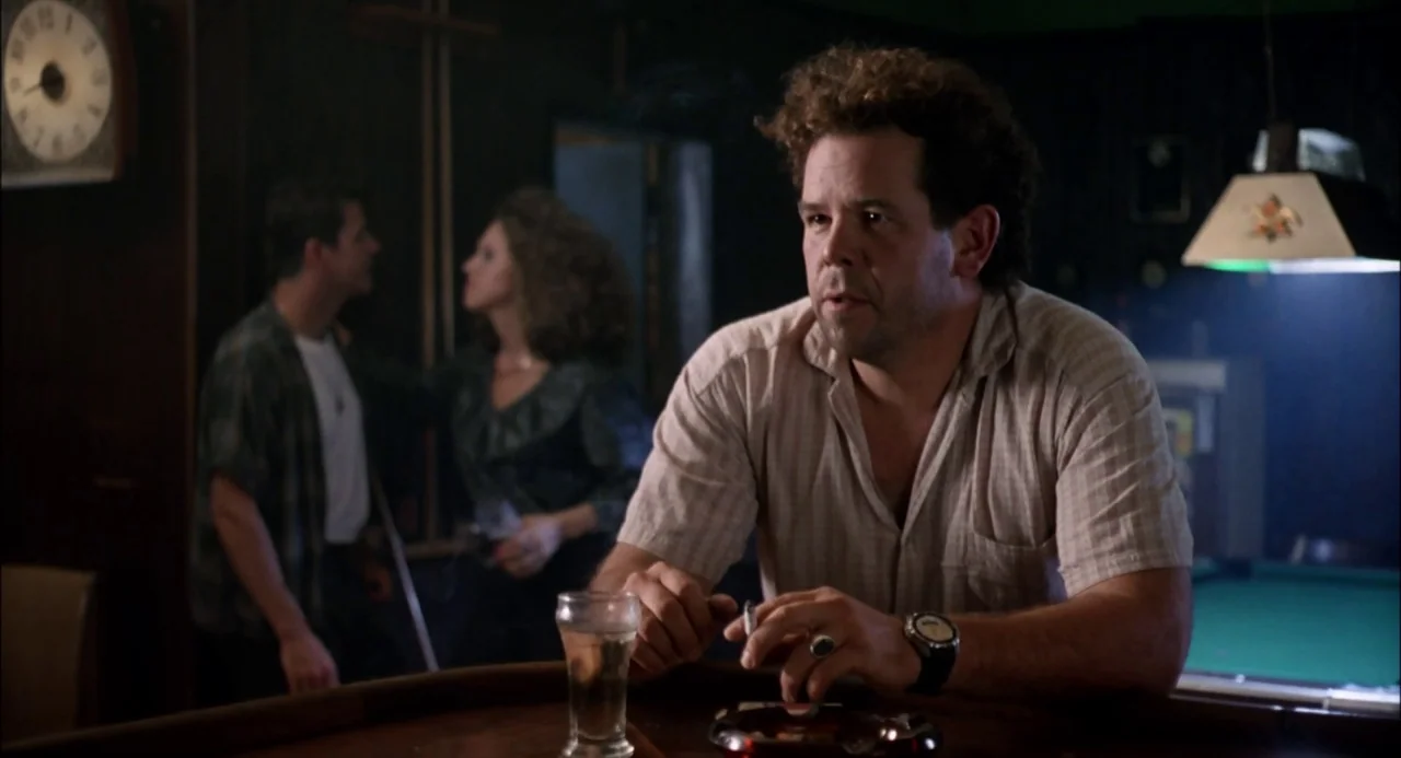 Trees Lounge (1996) movie still: medium — A dark tavern interior features a wooden counter and a pool table nearby. A man with curly hair sits at…