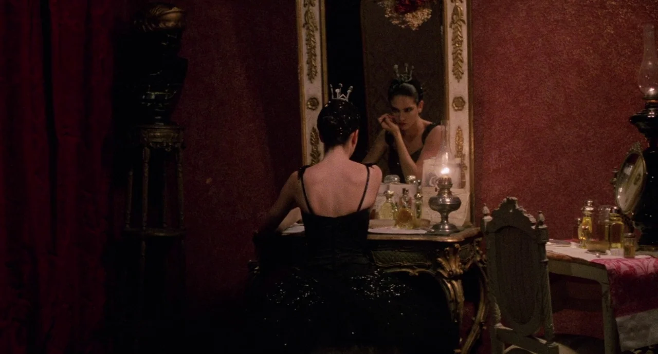 Etoile (1989) movie still: medium — A dimly lit room features a gold-trimmed antique vanity with velvet-textured dark red walls. A young woman in a…