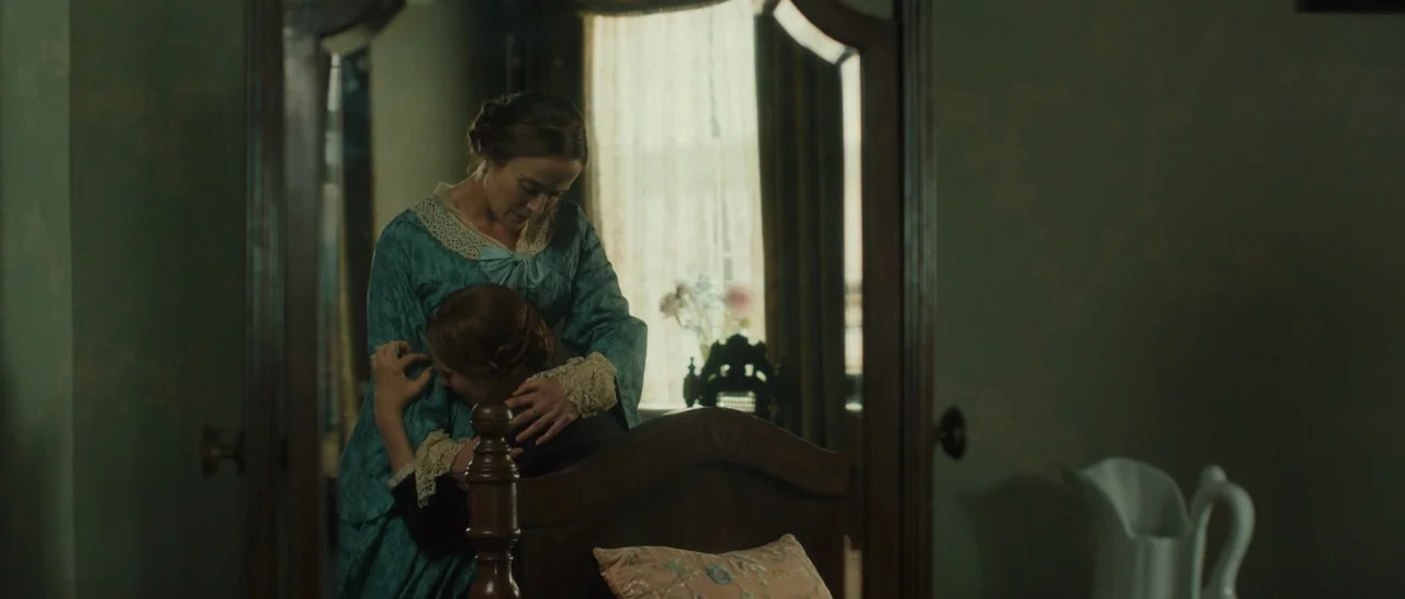 A Quiet Passion (2016) movie still: medium — A 19th-century bedroom features green wallpaper and a heavy wooden bed frame. A woman in a teal dress…