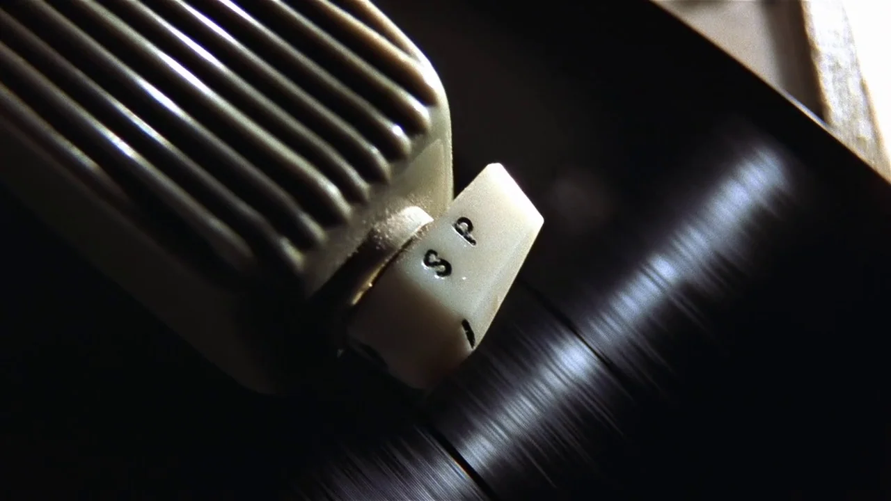 Almost Famous (2000) movie still: closeup — A close view of a vintage magnetic tape recorder mechanism with a speed toggle. The plastic head is…