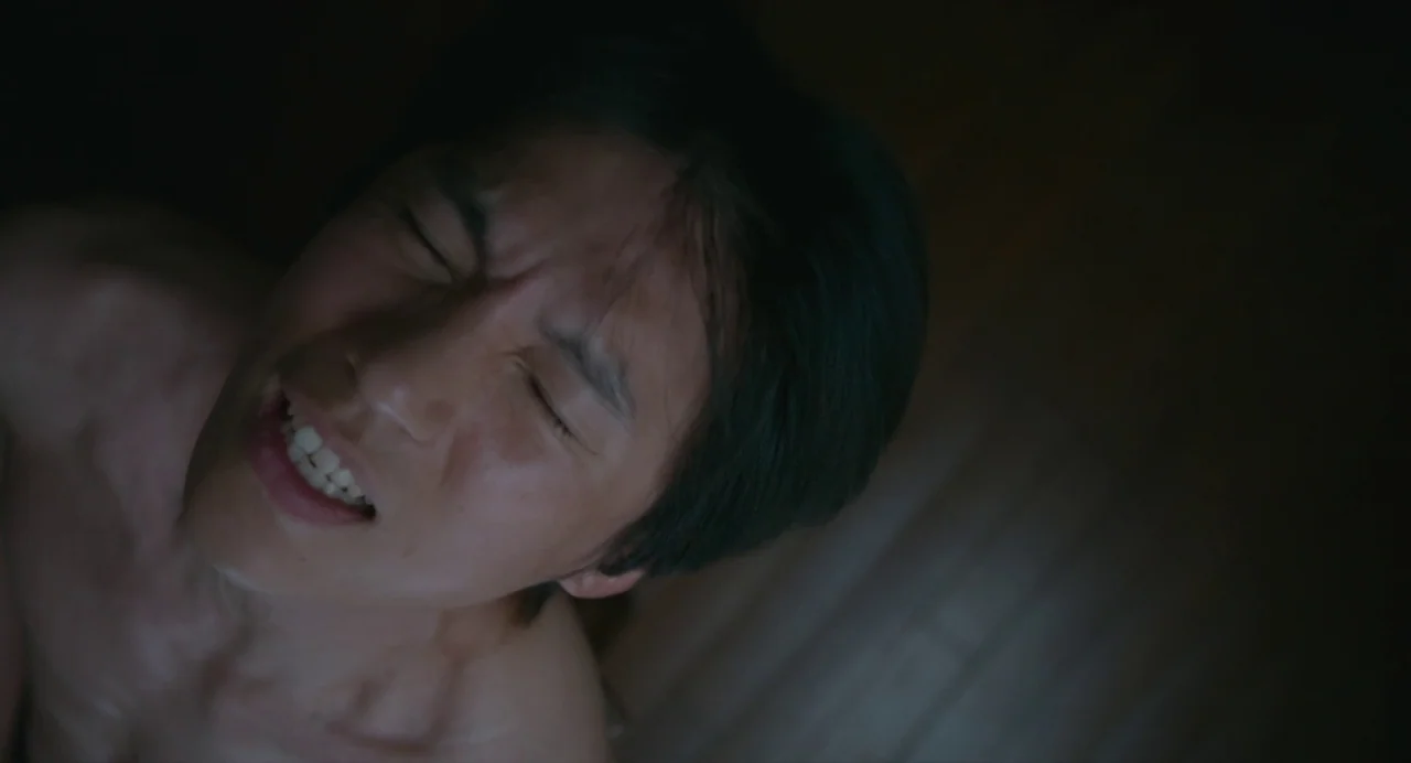 White River (2023) movie still: closeup — A dark, dimly lit room with wooden surfaces visible in the blurry background. A shirtless man has his head…