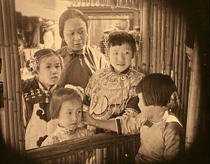 Broken Blossoms (1919) movie still: medium — An adult woman and four children stand behind a bamboo slatted barrier. The children look toward each…