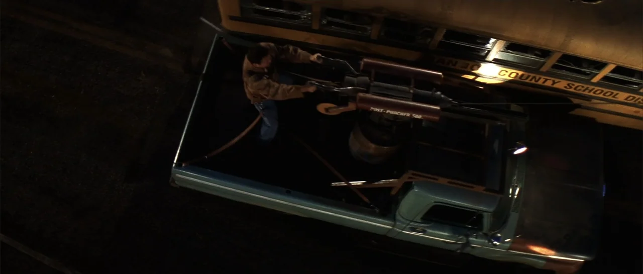 Jeepers Creepers 2 (2003) movie still: wide — An overhead view shows the bed of a pickup truck at night. A man operates a large mechanical device…