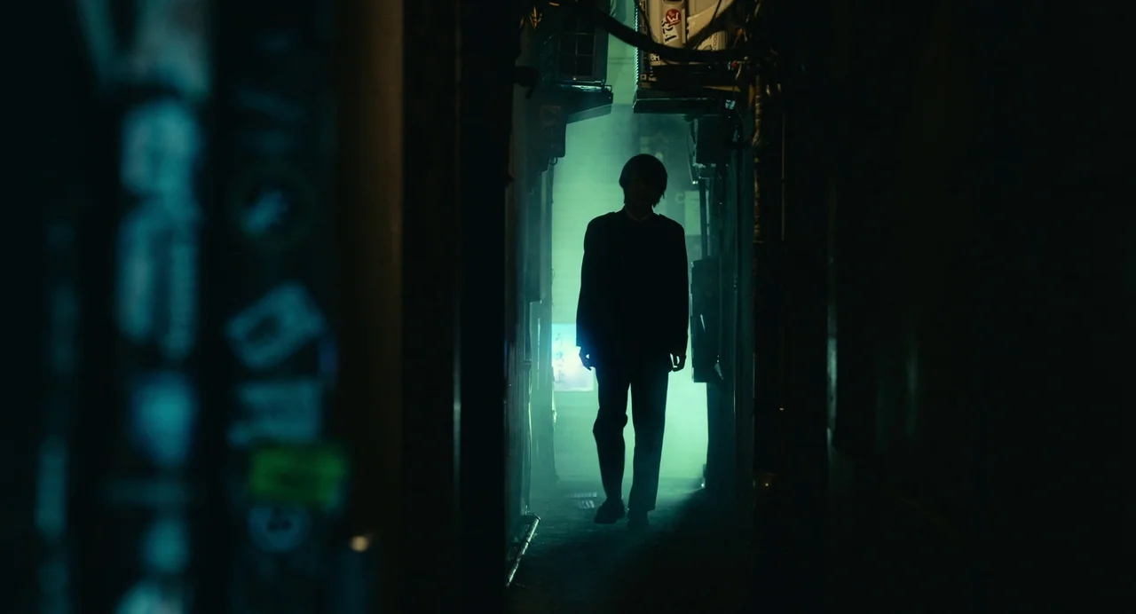 xxxHolic (2022) movie still: fullbody — A narrow, dark urban passageway is filled with mist and backlit by neon light. A slender man moves forward…