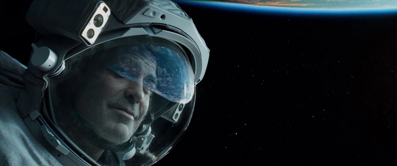 Gravity (2013) movie still: closeup — An astronaut in a pressurized suit floats against the vast dark void of space. The curve of the earth is…