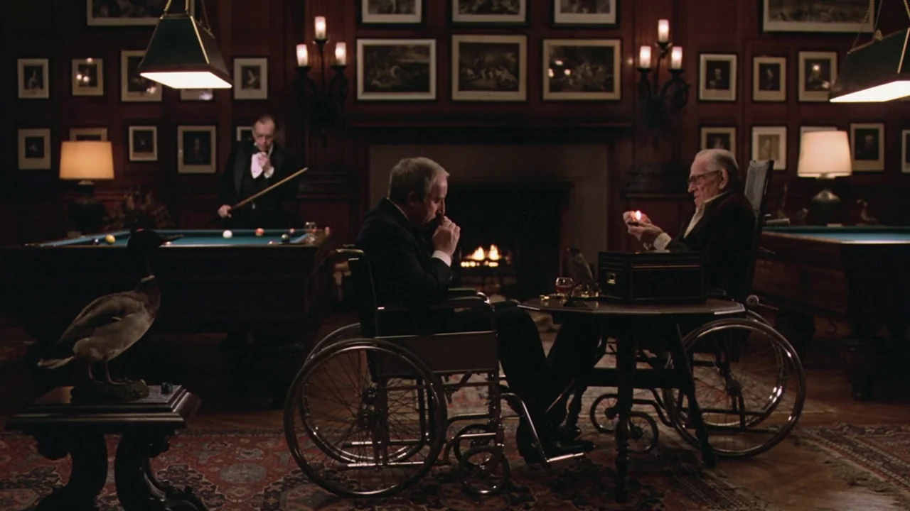 Being There (1979) movie still: wide — A dark paneled billiard room features a fireplace, two pool tables, and framed pictures. Two men in…