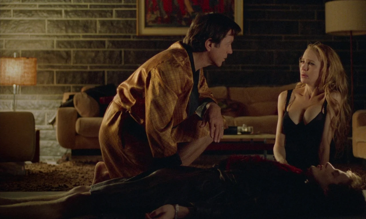 Water Drops on Burning Rocks (2000) movie still: medium — A dark living room features a stone block wall and vintage mid-century furniture. A man in…