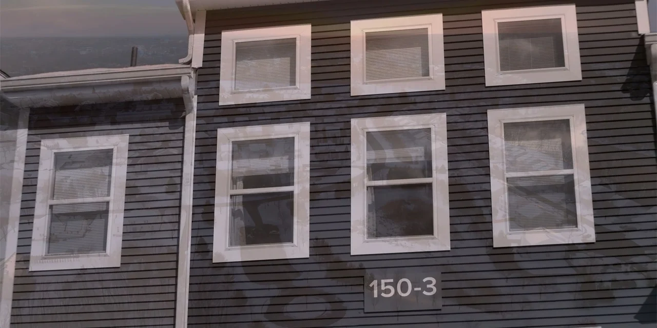 About Fate (2022) movie still: establishing — A multi-story building exterior features dark grey horizontal siding and multiple white-framed…
