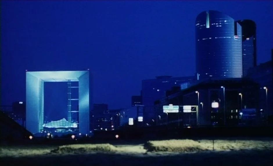 Simon, The Magician (1999) movie still: establishing — A view of the La Défense district at night under a deep blue sky. The Grande Arche de la…