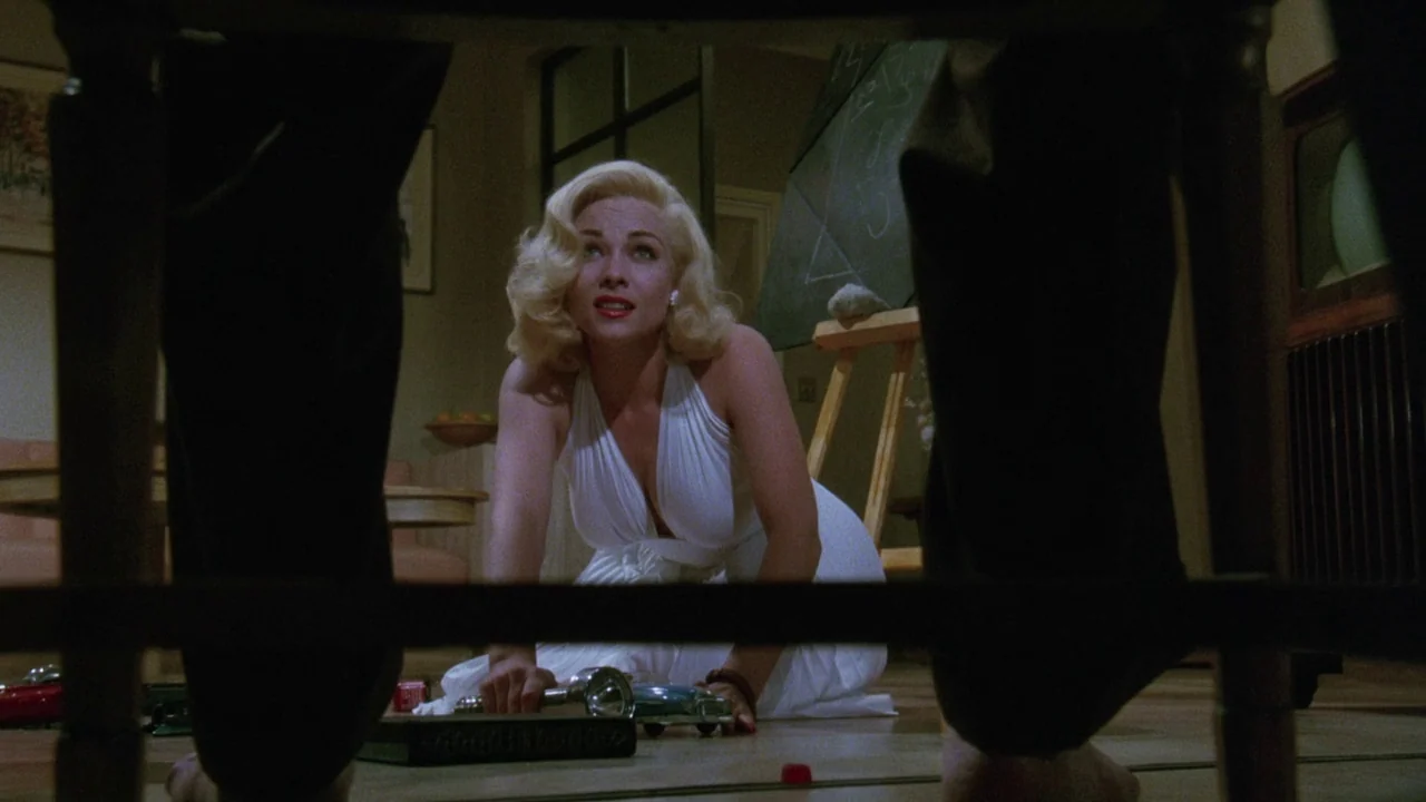 Insignificance (1985) movie still: medium — A dimly lit room features a wooden easel and a television set in the background. A woman in a white…